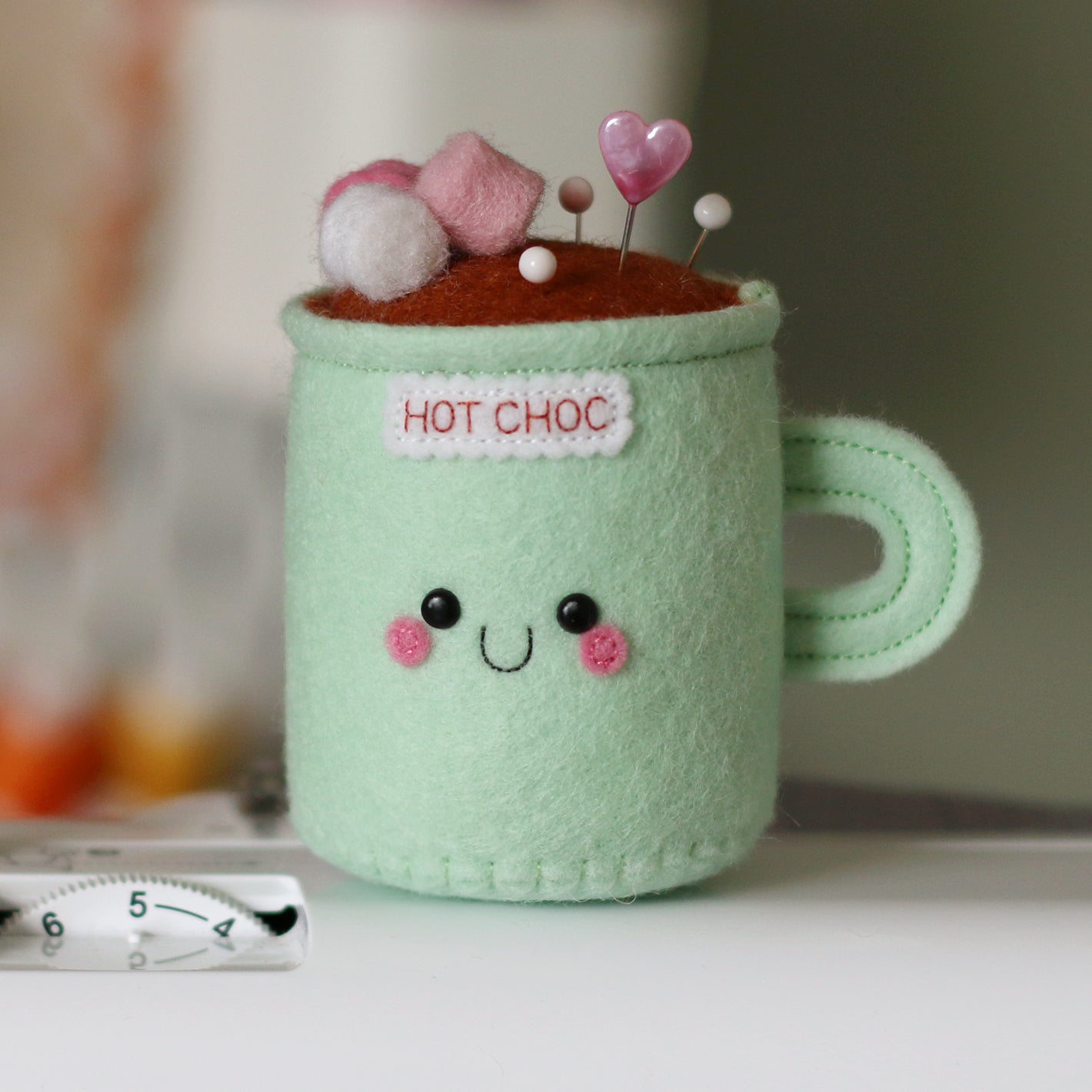 Pincushion mug labeled 'Hot Choc' with a face, sitting on a sewing machine.