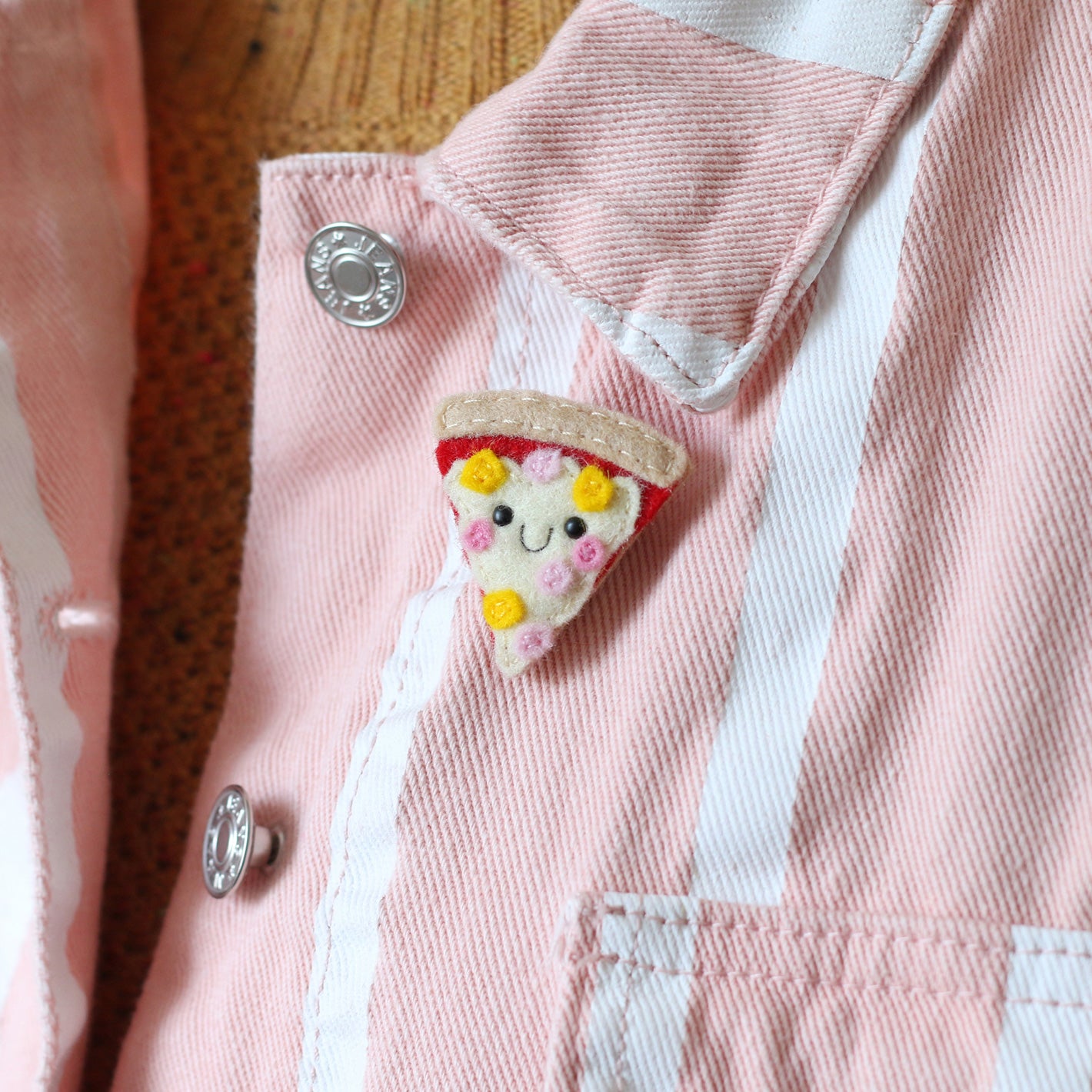 ham and pineapple pizza felt brooch modelled on a pink and white striped denim jacket
