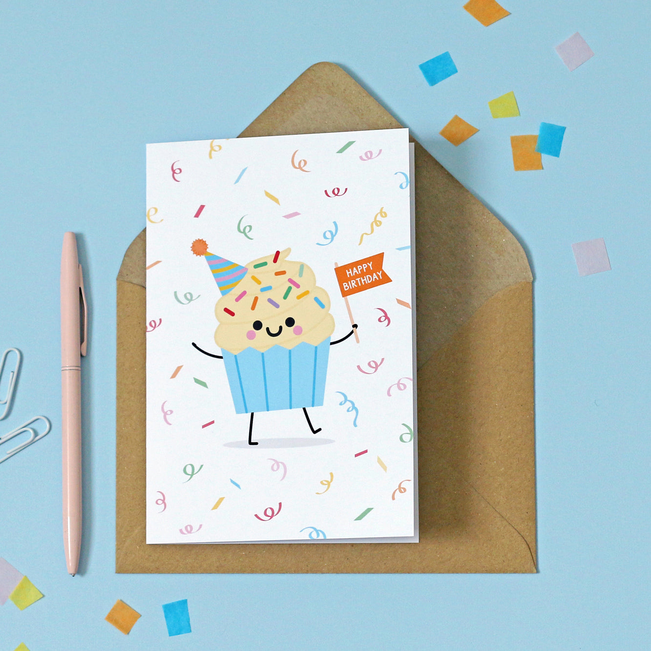 greeting card featuring a happy vanilla cupcake holding an orange flag with 'HAPPY BIRTHDAY' on it, surrounded by illustrated confetti