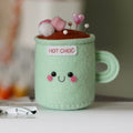 Pincushion mug labeled 'Hot Choc' with a face, sitting on a sewing machine.
