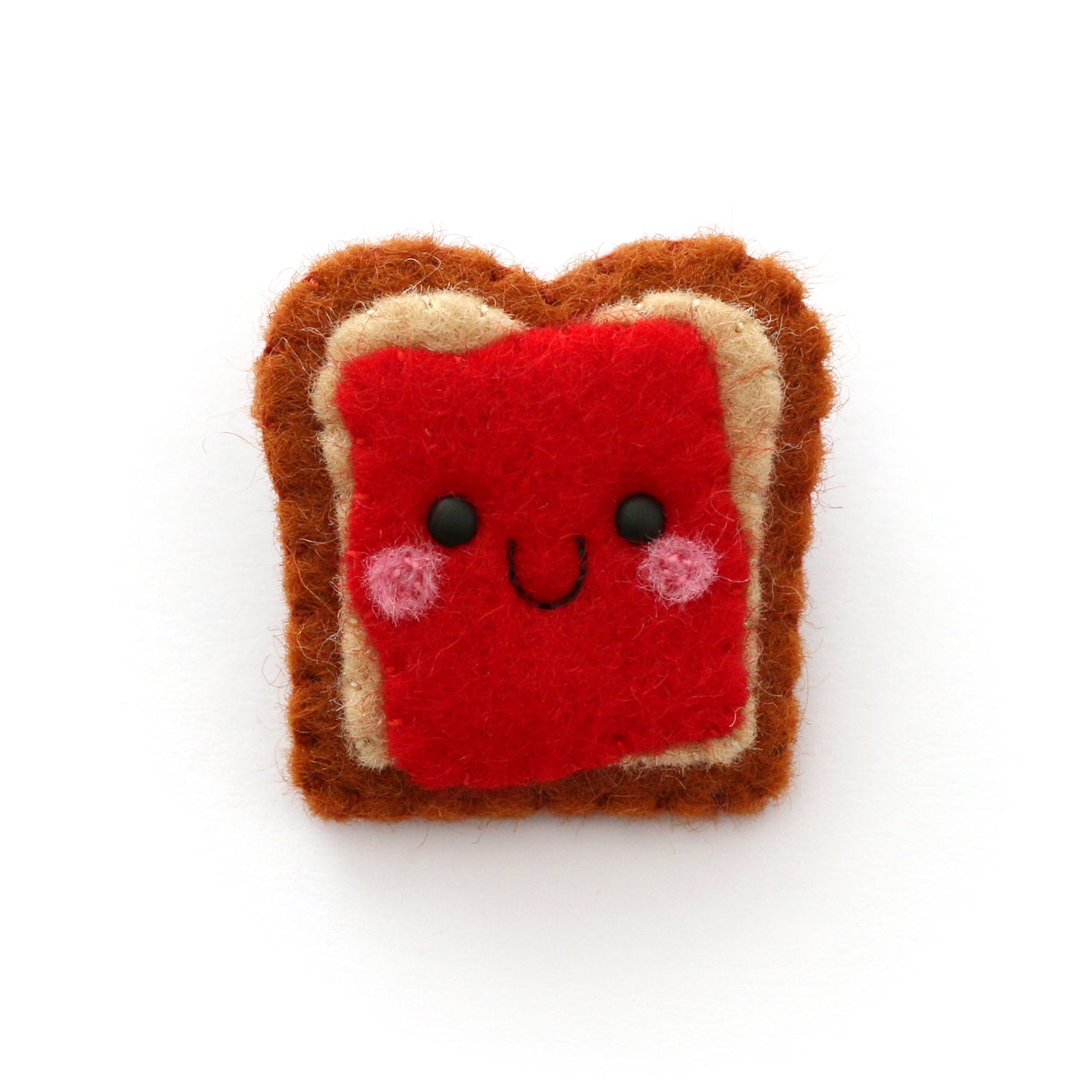 A cute felt pin shaped like a slice of toast with red jam and a smiling face, set against a plain white background.