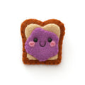 A cute felt pin shaped like a slice of bread with purple jelly on it, set against a plain white background.