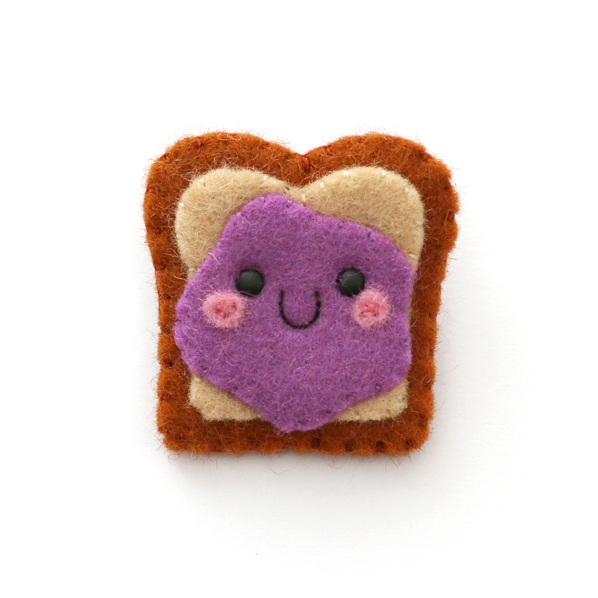 A cute felt pin shaped like a slice of bread with purple jelly on it, set against a plain white background.