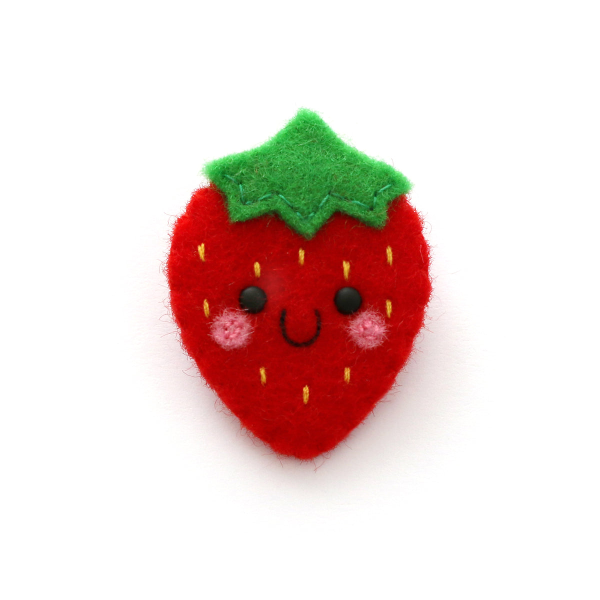 A cute, handmade strawberry brooch with a smiling face, pink cheeks, and a green leafy top, shown on a plain white background.