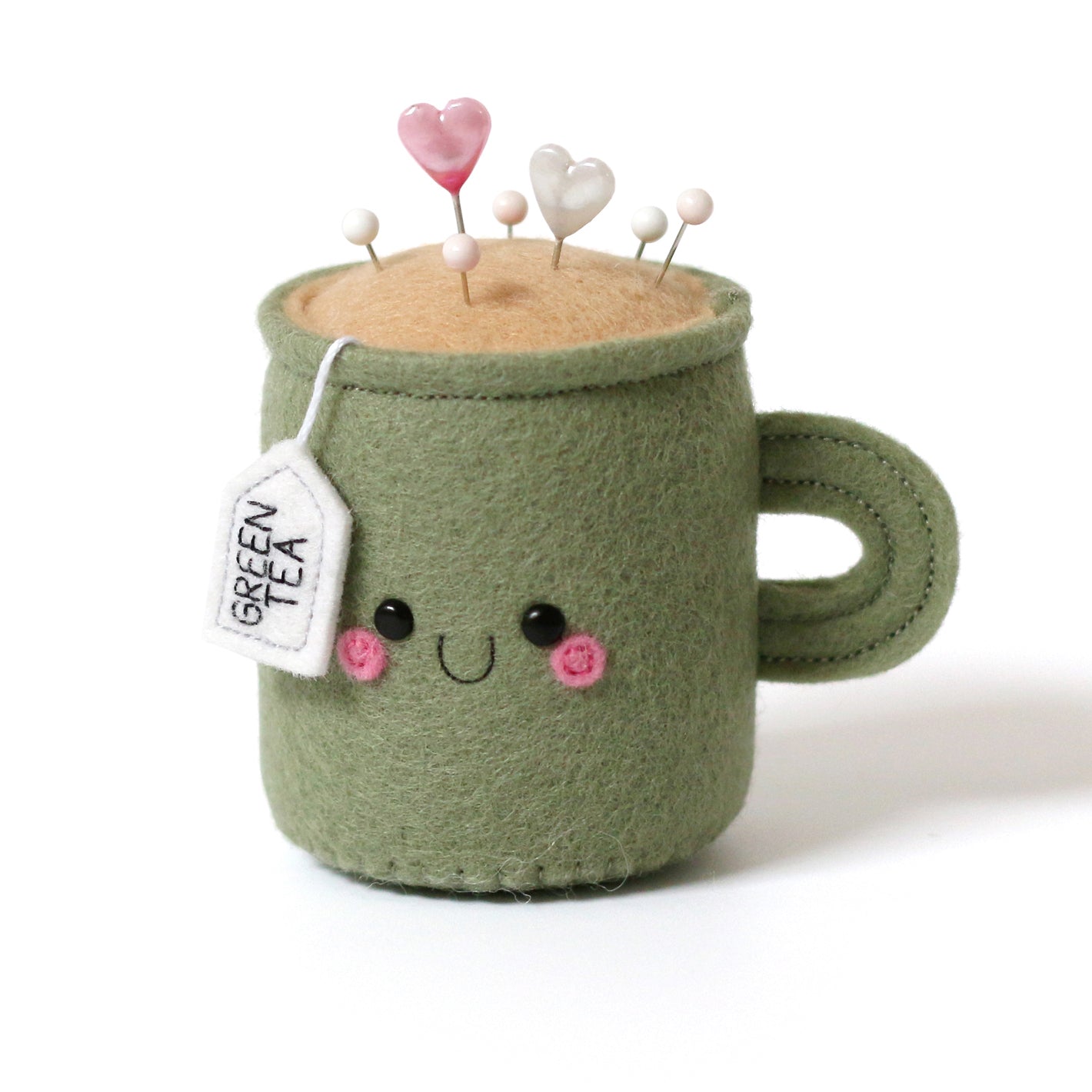 Green felt mug with a face, green tea bag, pincushion on a white background