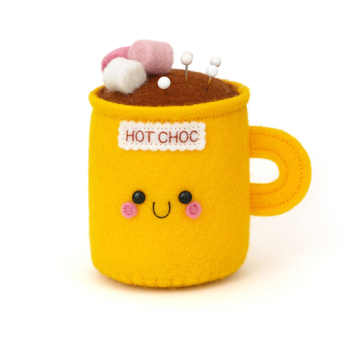A cute yellow felt hot chocolate mug pin holder with embroidered facial features, pink cheeks, a 'HOT CHOC' label, brown felt cocoa surface, and pink and white felt marshmallows on top, photographed on a clean white background.