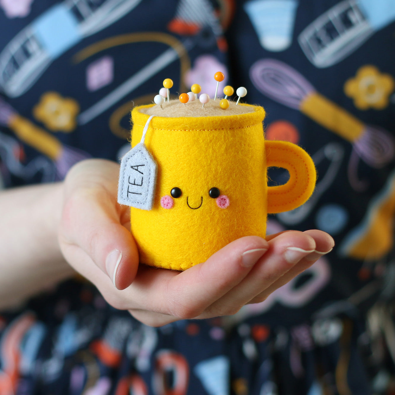 Person holding a bright yellow teacup pincushion