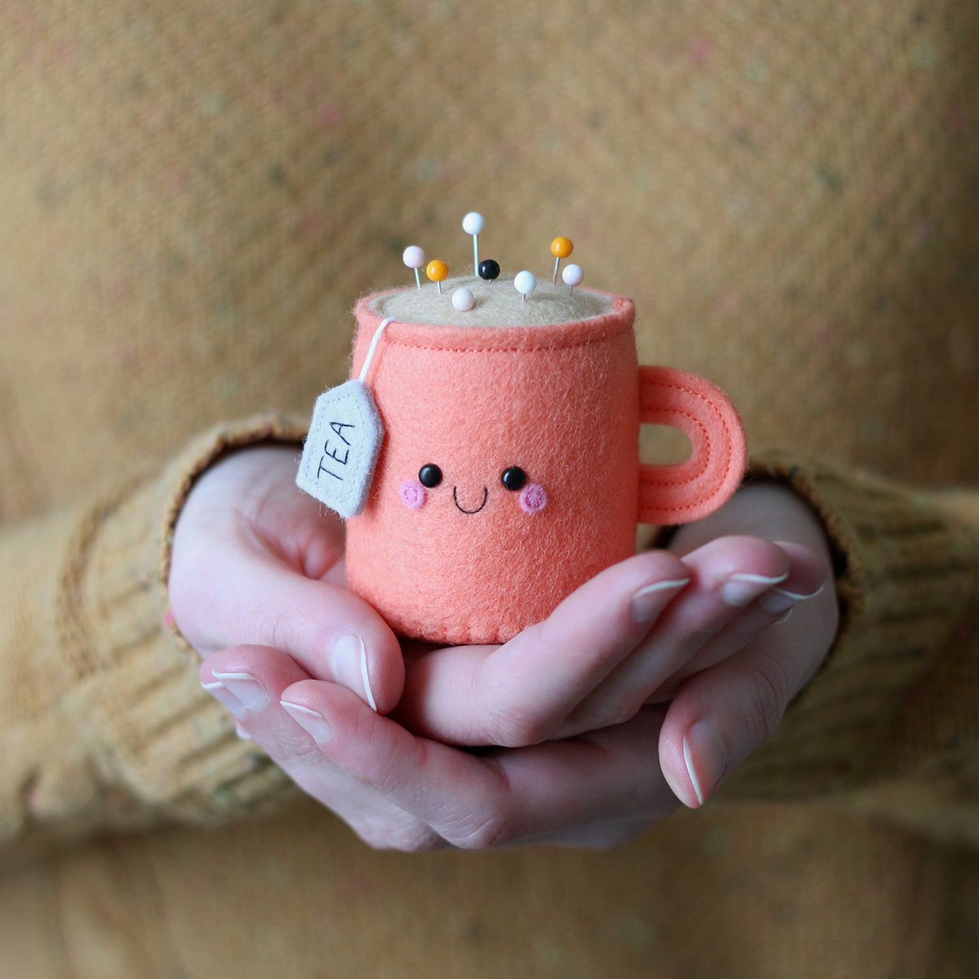 Hands holding cute coral shade teacup pincushion by hannahdoodle